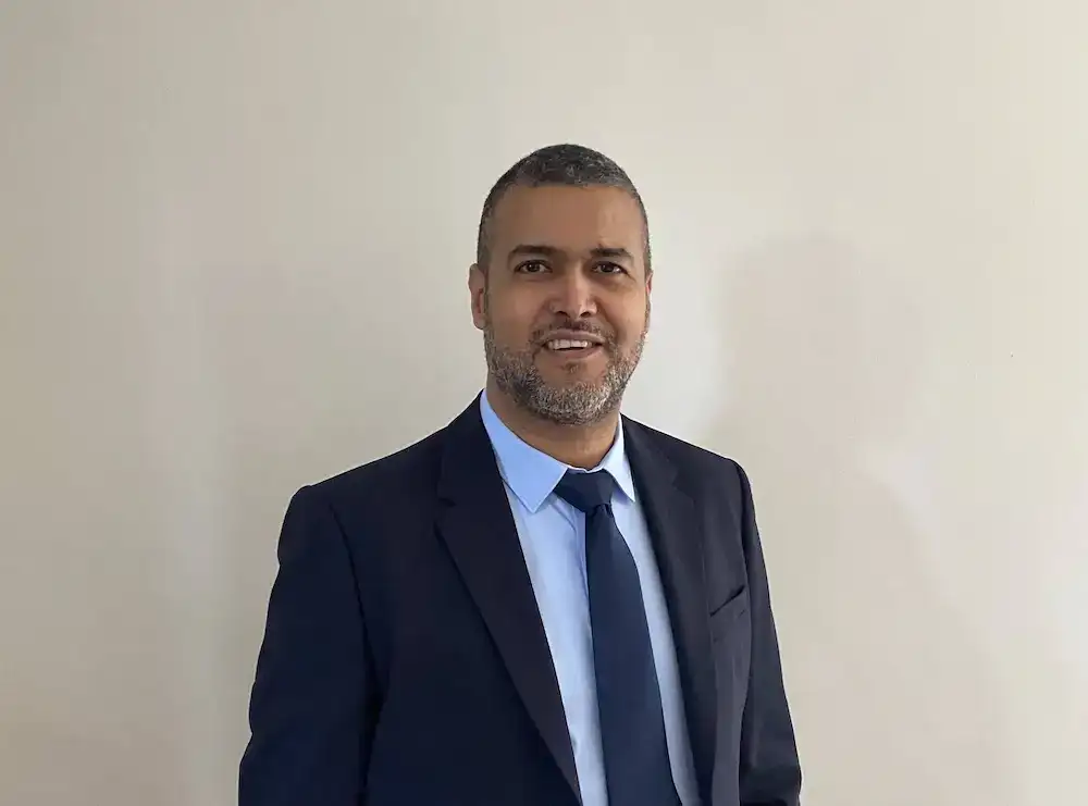 Homme d'affaires en costume élégant pour réseau professionnel, visage souriant, fond neutre blanc.